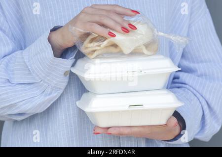 Mani di donna che tengono scatole da pranzo in schiuma da asporto. Contenitori per alimenti monouso, primo piano. Foto Stock