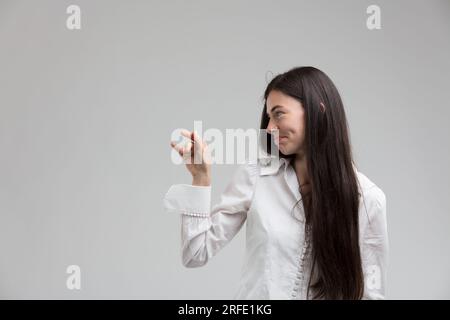 Con un leggero imbarazzo mescolato con curiosità, una giovane donna guarda lateralmente, facendo un gesto come toccare, ma non completamente fiduciosa. Sembra di sì Foto Stock