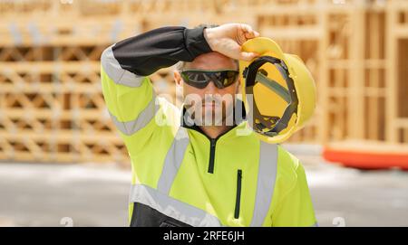 Lavoratori stanchi e sovraccarichi di lavoro nella costruzione di uniformi sullo sfondo della costruzione di edifici. Costruttore nel cantiere. Uomo lavoratore con casco su costru Foto Stock