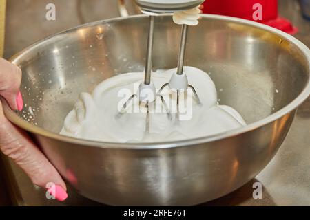 Lo chef prepara gli albumi con il mixer nel recipiente. Foto Stock