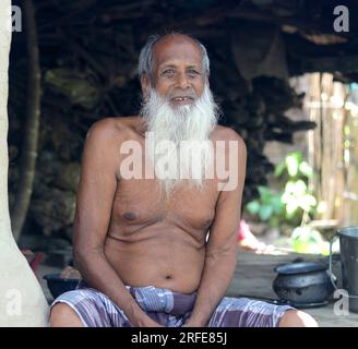 Un vecchio povero con una lunga barba bianca seduto sulla sua casa di fango del villaggio. Foto Stock