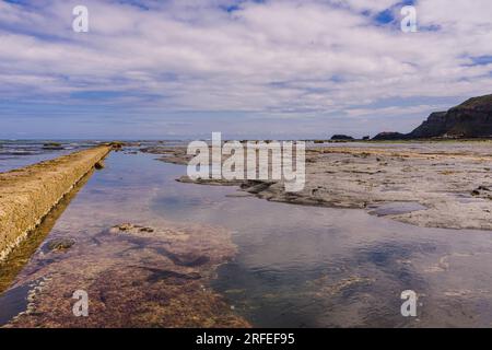 Con la bassa marea sulla East Beach a Whitby, è esposta una grande area di rocce piatte e piscine rocciose. Questa foto è stata scattata guardando verso Saltwick NAB - il wh Foto Stock