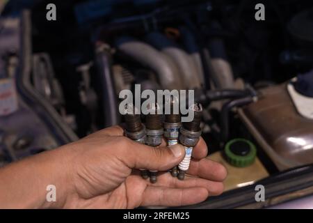 Primo piano di una mano con quattro candele usate sullo sfondo del motore. Concetto di riparazione auto Foto Stock