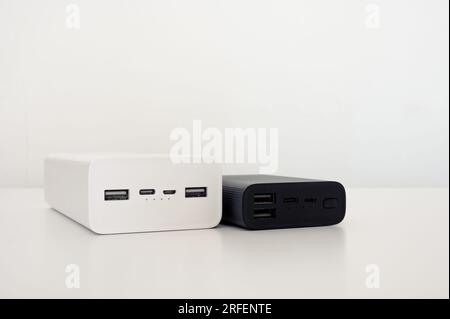 Power Bank bianco e caricabatterie mobile nero sul tavolo. Sfondo bianco. Foto Stock