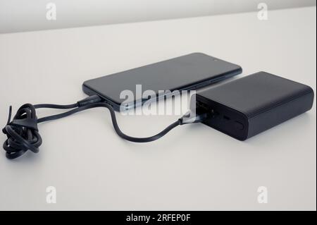 Black Power Bank addebita il cellulare. Cavo nero. Entrambi su sfondo bianco Foto Stock