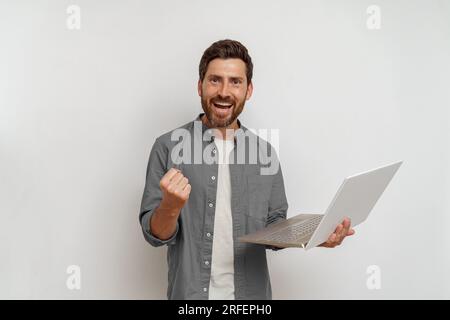 Felicissimo uomo che tiene un notebook con pugno rialzato trionfale su sfondo bianco Foto Stock