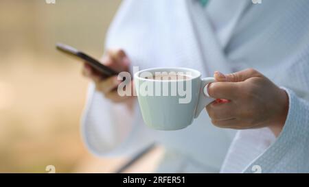 Le mani femminili tengono il caffè in tazza e il telefono cellulare a casa per primo piano Foto Stock