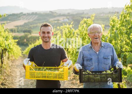 Lavoratori multigenerazionali che raccolgono uva per la produzione vinicola oganica - tradizione, stile di vita agricolo e concetto di piccola impresa - Focus sui volti Foto Stock