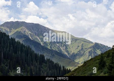 Paesaggi montuosi con colline verdi e un cielo blu con nuvole sparse nel Parco Nazionale di Ile-Alatau, Kazakistan Foto Stock