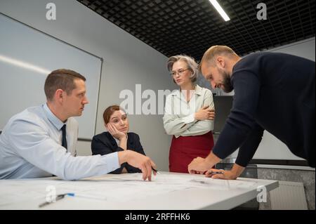 L'estrusione femminile valuta il lavoro dei subordinati. Progettisti ingegneri a una riunione. Foto Stock