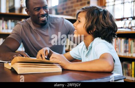 insegnante di scuola che insegna a un ragazzo in una biblioteca. Insegnante elementare maschile che assiste un giovane studente con il suo lavoro scolastico. Lettura e scrittura private Foto Stock