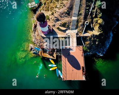 Foto aerea con droni dall'alto verso il basso di un gruppo di persone in piedi su tavole da paddle nel lago verde Kapchagay vicino al faro in Kazakistan Foto Stock