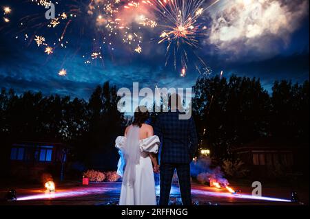 sposi e sposi stanno con le spalle sullo sfondo di fuochi d'artificio festivi il giorno delle nozze la sera Foto Stock