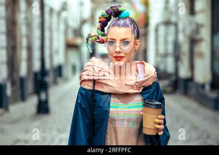 Giovane ragazza divertente e stravagante con piercing e capelli pazzi goditi il caffè da asporto per strada: Donna Hipster dal look trendy e colorato all'avanguardia che si diverte Foto Stock