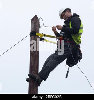 Tecnico che collega il cavo in fibra ottica a banda larga a un palo Foto Stock