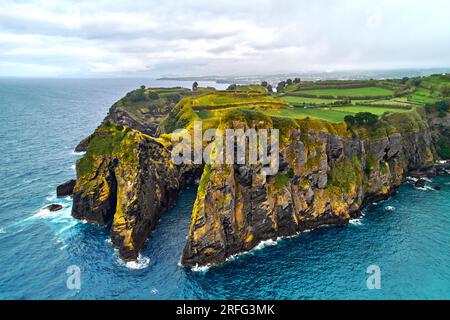 Foto aerea, punto di vista con droni, surf nell'Oceano Atlantico, costa rocciosa e terreni agricoli dell'Isola di Ponta Delgada. Sao Miguel, Azzorre, Portogallo. Bella n Foto Stock