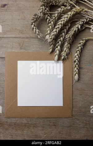 carta bianca per note su una busta marrone con orecchie di grano su fondo di legno Foto Stock