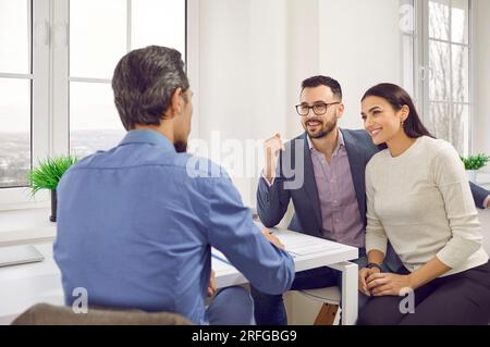 Clienti giovani e felici che parlano con un agente immobiliare o un broker in ufficio Foto Stock