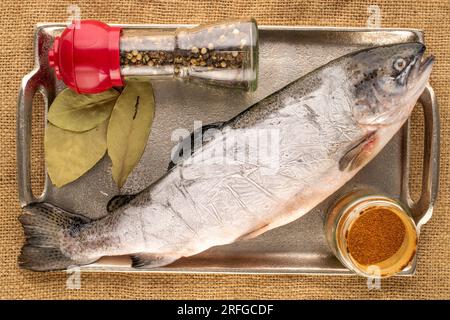 Una trota congelata con vassoio di metallo, pepe caldo e foglia di alloro su tavolo di legno, macro, vista dall'alto. Foto Stock