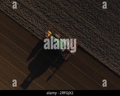 Un trattore John Deere semina un campo precedentemente coltivato con mais dolce, in tarda serata. Foto Stock