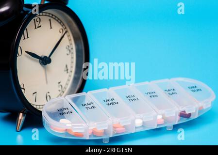 Contenitore in plastica con pillole e sveglia nera su sfondo blu Foto Stock