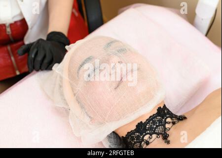 Un estetista mette una garza sul viso del paziente, curando la pelle secca e sensibile. Foto Stock