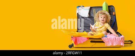 Graziosa bambina seduta in valigia con oggetti personali su sfondo giallo con spazio per il testo Foto Stock
