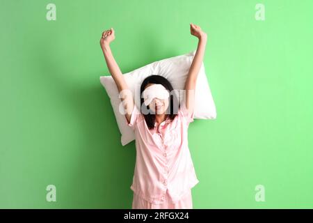 Bella donna asiatica in pigiama con cuscino su sfondo verde Foto Stock