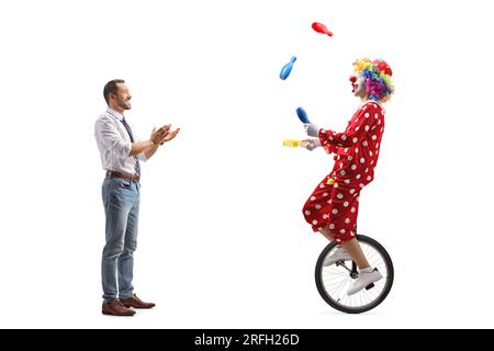 Foto a lunghezza intera di un giovane che guarda un clown su un triciclo e applaude con le mani isolate su sfondo bianco Foto Stock