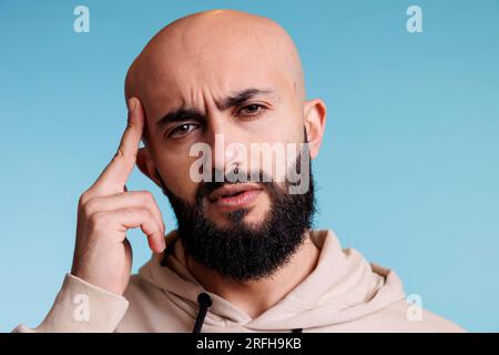 L'uomo arabo sfrega il tempio mentre soffre di un ritratto di attacco di emicrania. Giovane adulto arabo con la barba calva che soffre di mal di testa e guarda la macchina fotografica Foto Stock