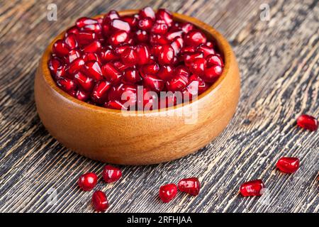 semi di melograno rossi maturi in un piatto, melograno rosso sbucciato in un piatto di legno sul tavolo Foto Stock