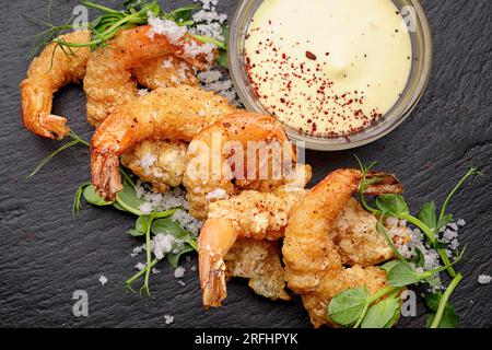 Gamberetti fritti in pastella con salsa, su ardesia nera, su fondo scuro Foto Stock