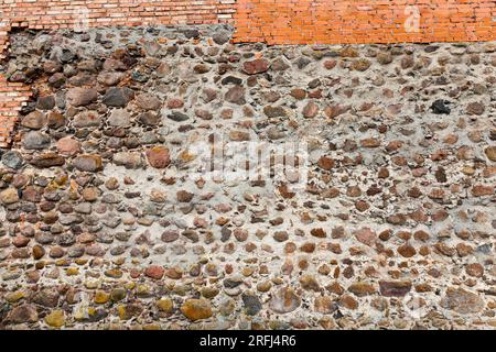 mura combinate di un antico castello, parte delle mura di un castello medievale fatto di pietre, ciottoli e mattoni rossi Foto Stock