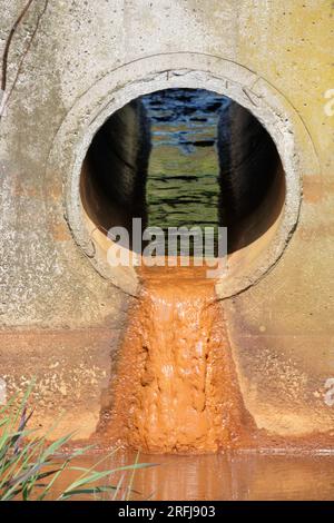 Acqua che scorre da un grande tubo di drenaggio industriale in una parete di cemento Foto Stock