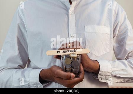 Un uomo tiene un bicchiere pieno di monete in rupie indiane, con la parola "pensionamento" scritta su un bastone Foto Stock