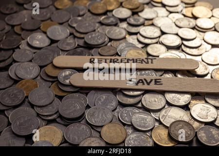 Una foto ravvicinata di monete in rupie indiane sparse su un tavolo, con la parola "pensionamento" scritta su un bastone Foto Stock