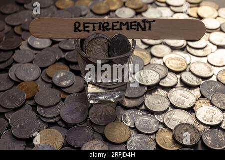 Un'immagine ravvicinata delle monete in rupie indiane sparse su un tavolo. La parola "pensionamento” è scritta in un bastone sul tavolo Foto Stock