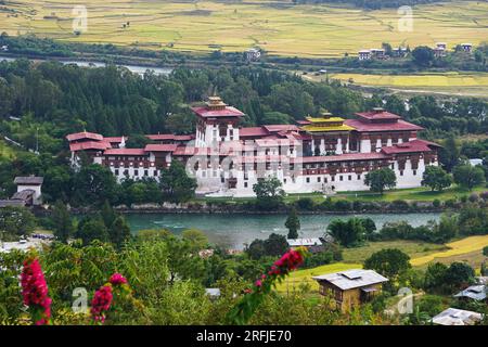 Ampia vista dello storico Punakha Dzong con il fiume Mo Chhu in primo piano e le verdi risaie terrazzate nella valle oltre il rurale Bhutan Foto Stock