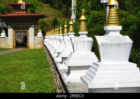 Una fila di stupa commemorativi identici imbiancati sormontati da guglie dorate sul terreno del Khamsum Yulley Namgyal Chorten nel Regno del Bhutan Foto Stock