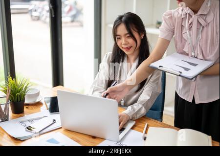 Un'attraente donna d'affari asiatica o una commercialista sta lavorando sui dati delle vendite aziendali finanziarie con il suo collega in ufficio. Foto Stock