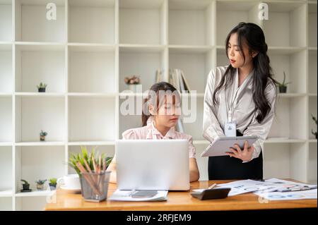 Due donne d'affari asiatiche concentrate o commercialisti stanno discutendo di lavoro, analizzando i dati di vendita e lavorando insieme in ufficio. Foto Stock