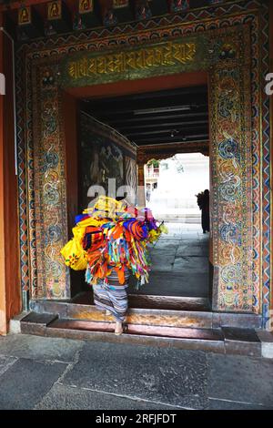 Hidden under a bundle of colorful fabric temple banners, a worker enters the ornate carved, painted doorway of Punakha Dzong in the Kingdom of Bhutan Stock Photo