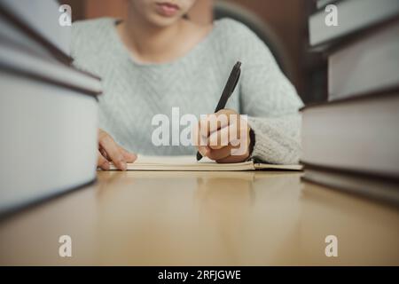 Studente che si prepara per il test universitario, esame, libro di lettura, libro di testo, scrittura di appunti, creazione di un riepilogo per il rapporto della classe. Tavolo di apprendimento sul posto di lavoro, h Foto Stock