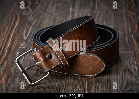 Cintura da uomo in pelle arrotolata con fibbia in metallo su scrivania in legno Foto Stock