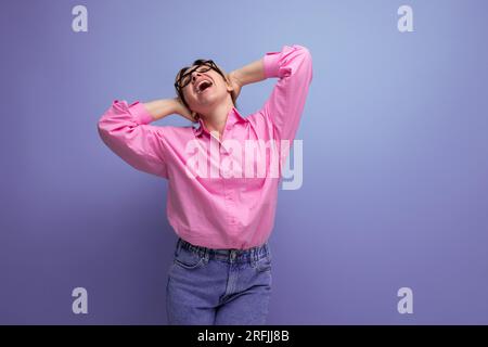 dreamy positivo giovane bionda modello donna caucasica con acconciatura ponytail in look elegante composto da blusa rosa e jeans Foto Stock