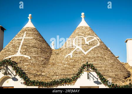 Alberobello, Italia - 1 gennaio 2023: Simboli di un cuore trafugato da una freccia raffigurante Santa Maria Addolorata dipinta sul tetto dei trulli Foto Stock