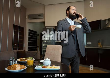 Maschio sta al tavolo con un telefono e un caffè Foto Stock
