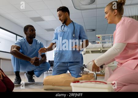 Medico maschio birazziale con diversi medici tirocinanti che imparano rcp su modello in ospedale Foto Stock