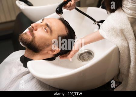 Il cliente gode della procedura di lavaggio dei capelli nel barbiere Foto Stock