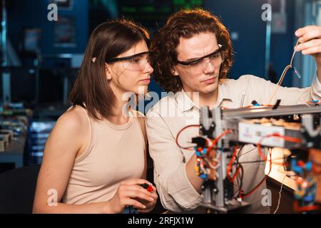 Giovane uomo e donna in occhiali protettivi che fanno esperimenti di robotica in laboratorio. Robot sul tavolo Foto Stock